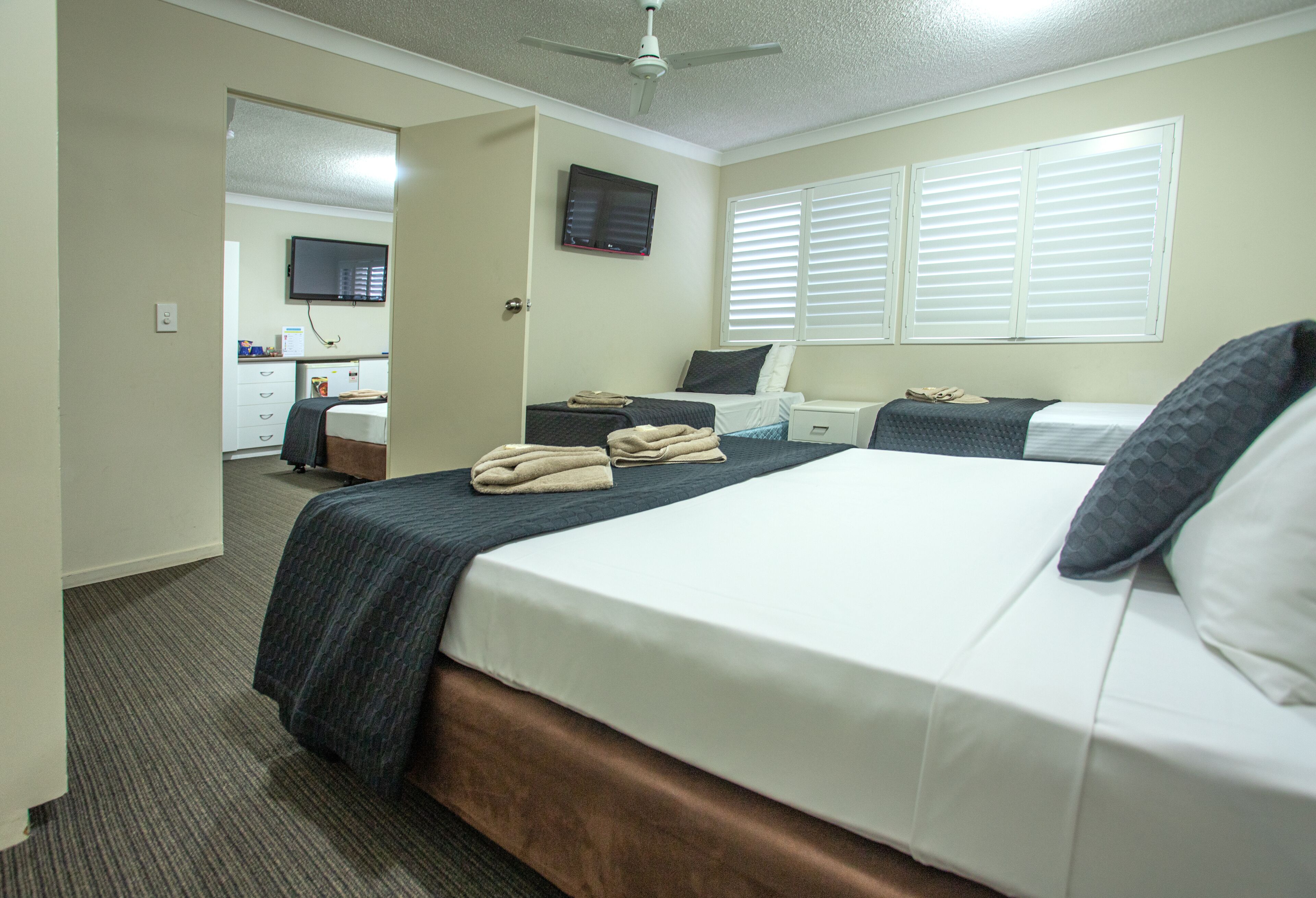 Quarto de hotel com uma cama grande, uma mesa de cabeceira, televisão na parede e janela com persianas.