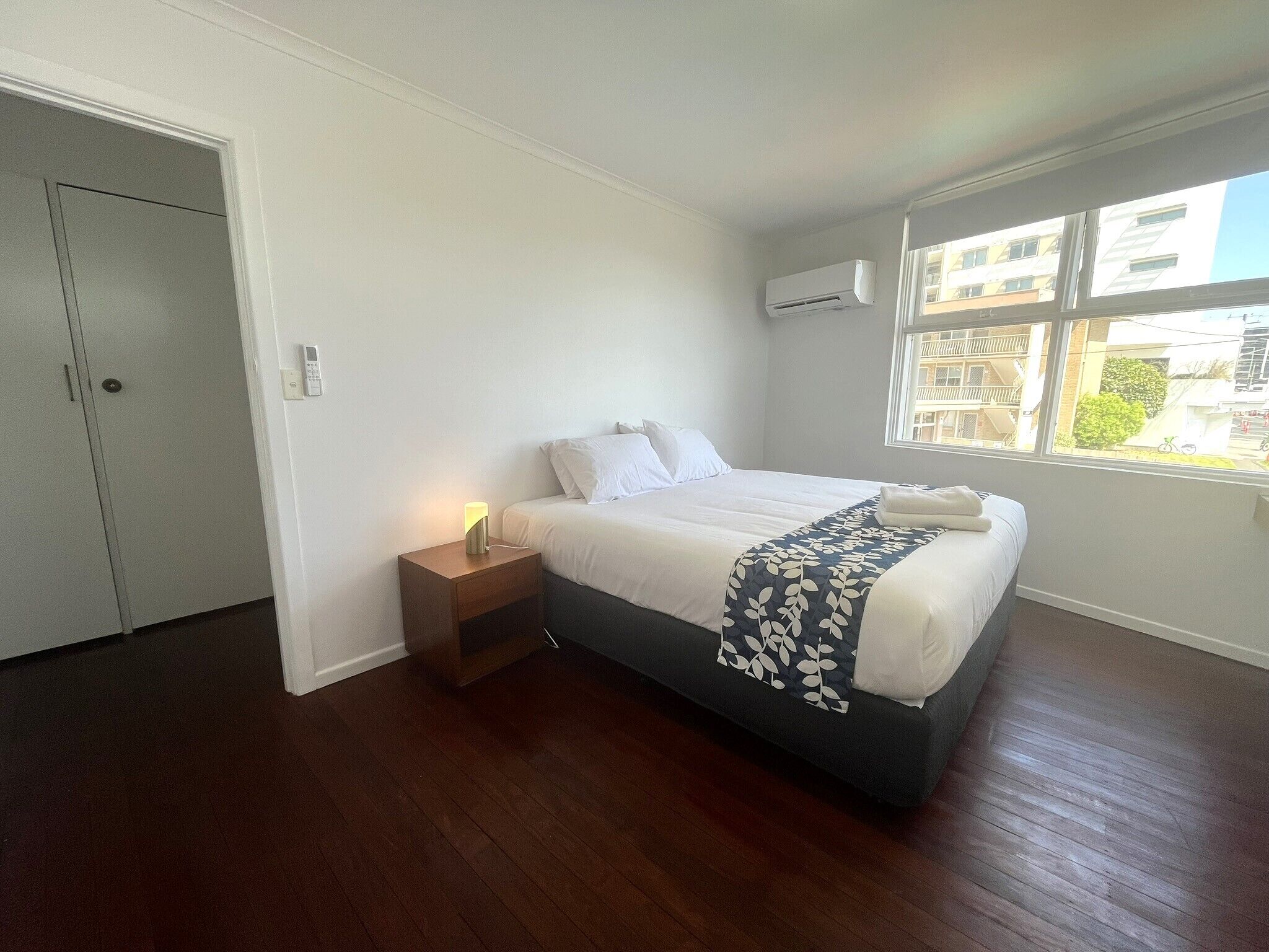 Una camera da letto con un letto, un comodino e una finestra che si affaccia su degli edifici.