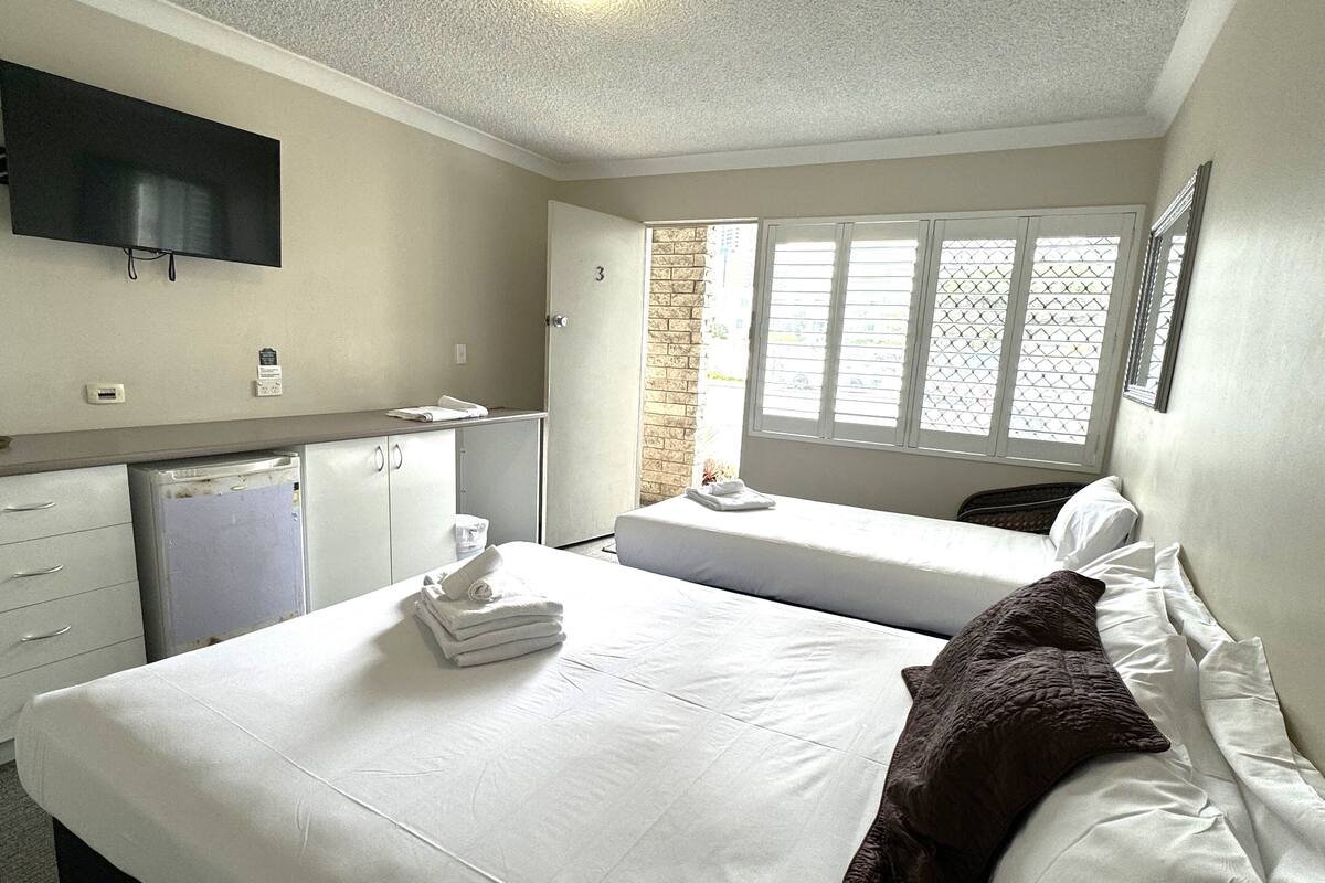 Ein Hotelzimmer mit Bett, Schreibtisch, Fernseher und einem Fenster mit Jalousien.