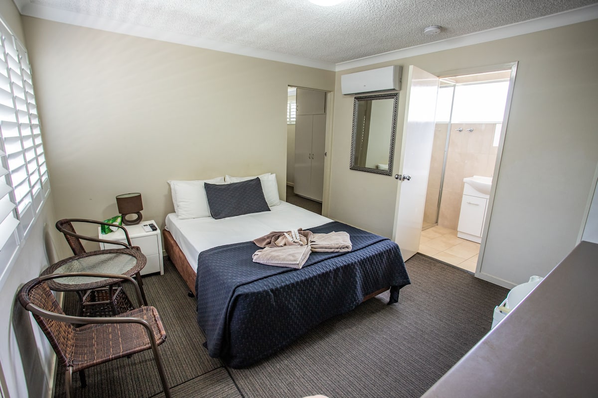Ein Hotelzimmer mit einem Bett, einem Sessel, einem Nachttisch, einem Spiegel und einer offenen Tür zum Badezimmer.