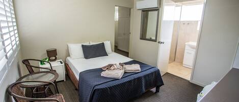 Habitación de hotel con cama, una silla, una mesita de noche, un espejo y una puerta abierta al baño.