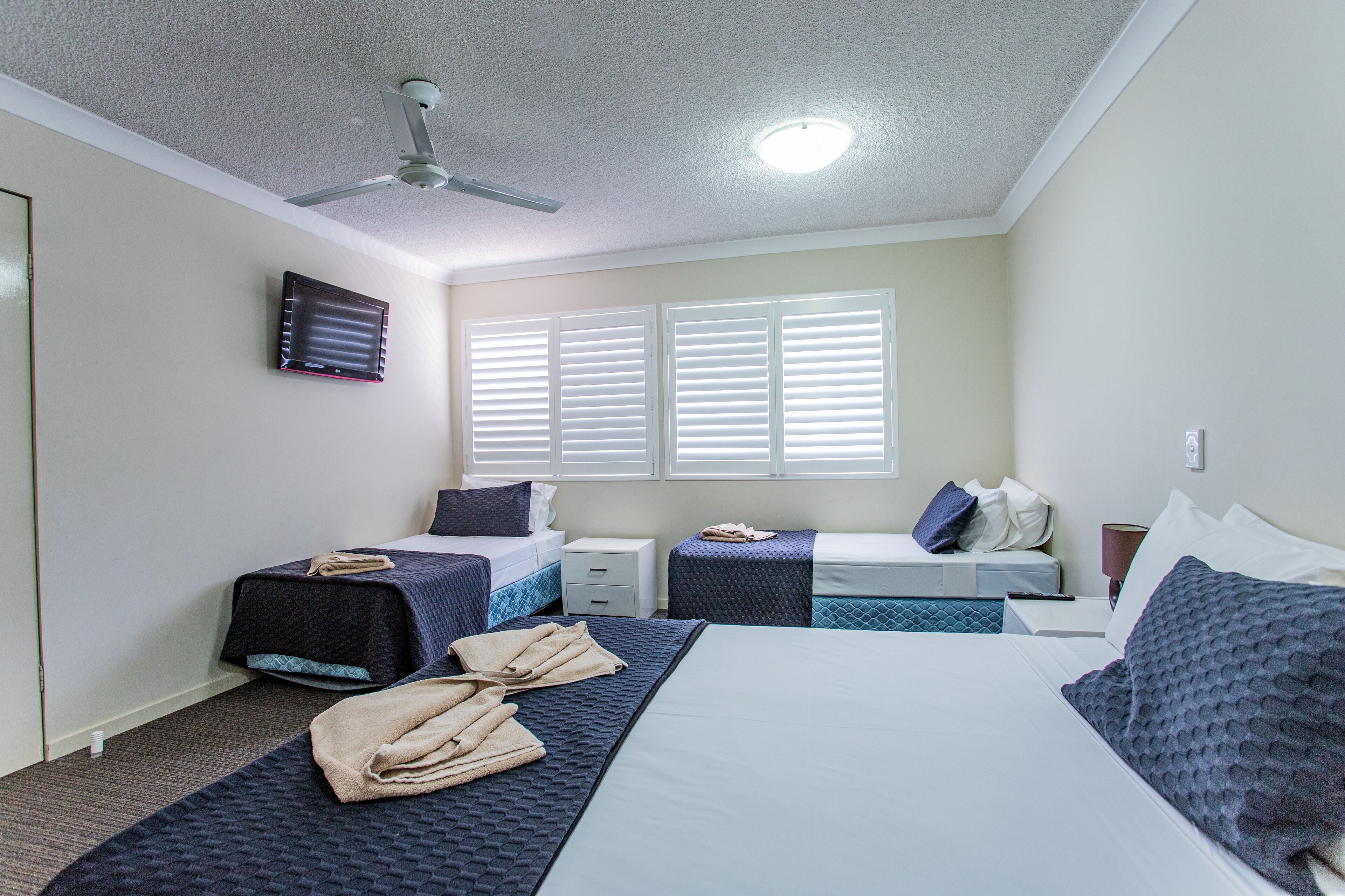 A hotel room with two beds, a ceiling fan, and a window with blinds.