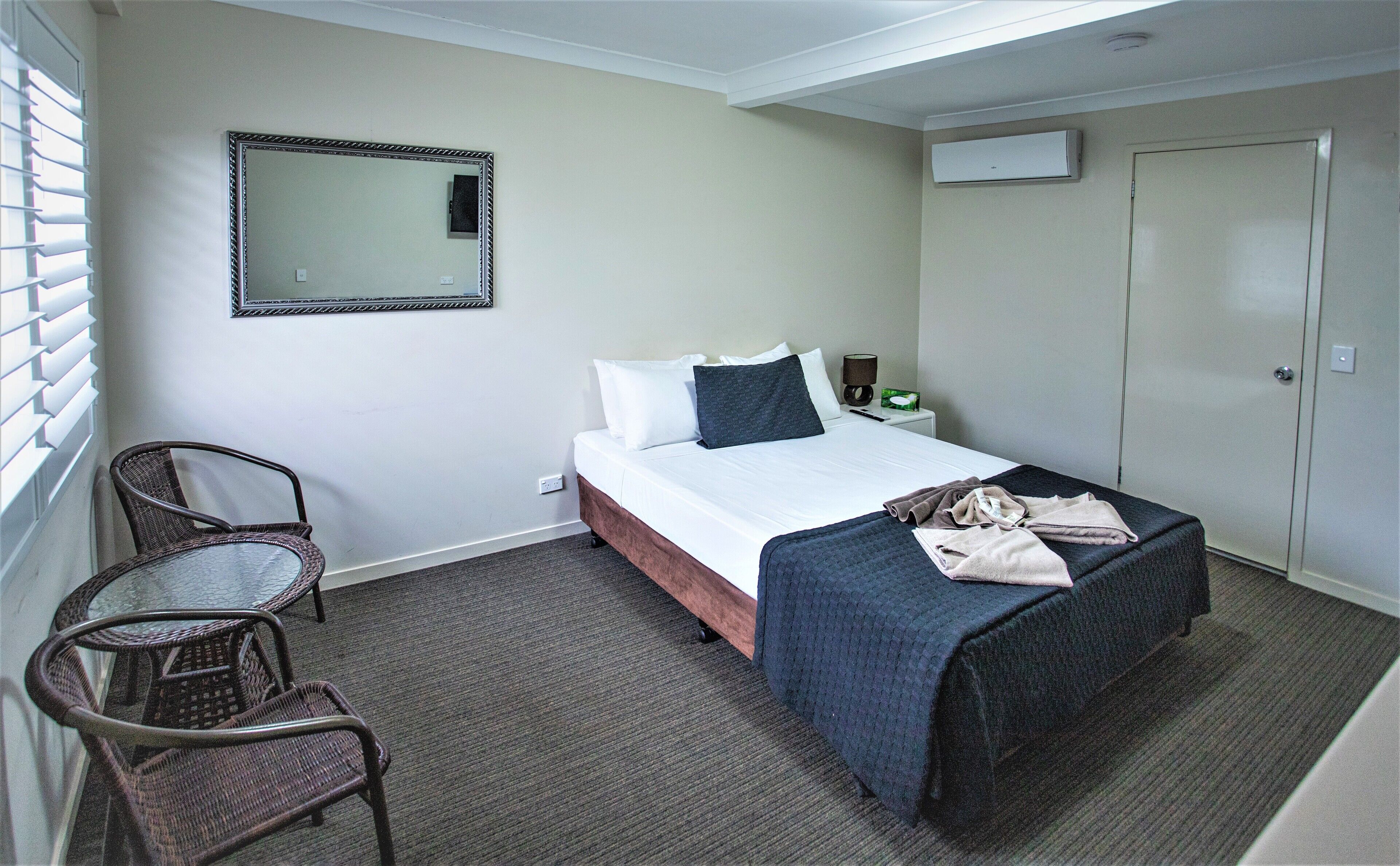 A hotel room with a bed, a chair, a bedside table with a lamp, a mirror, and a wardrobe.