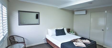 A hotel room with a bed, a chair, a bedside table with a lamp, a mirror, and a wardrobe.