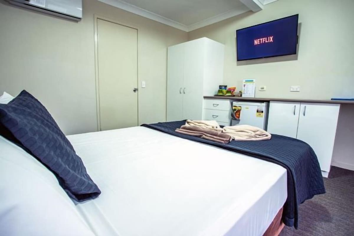 A hotel room with a bed, a desk, a television, and a wardrobe.