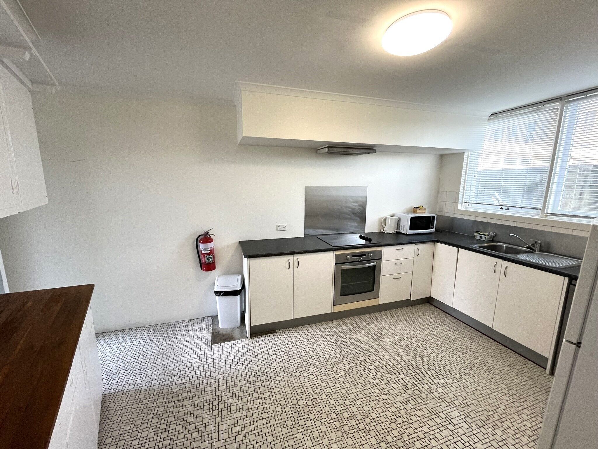 A compact kitchen with white cabinets, a microwave, a sink, and a fire extinguisher.
