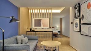 Una habitación de hotel moderna con sofá, una mesa redonda, un escritorio y obras de arte en las paredes.