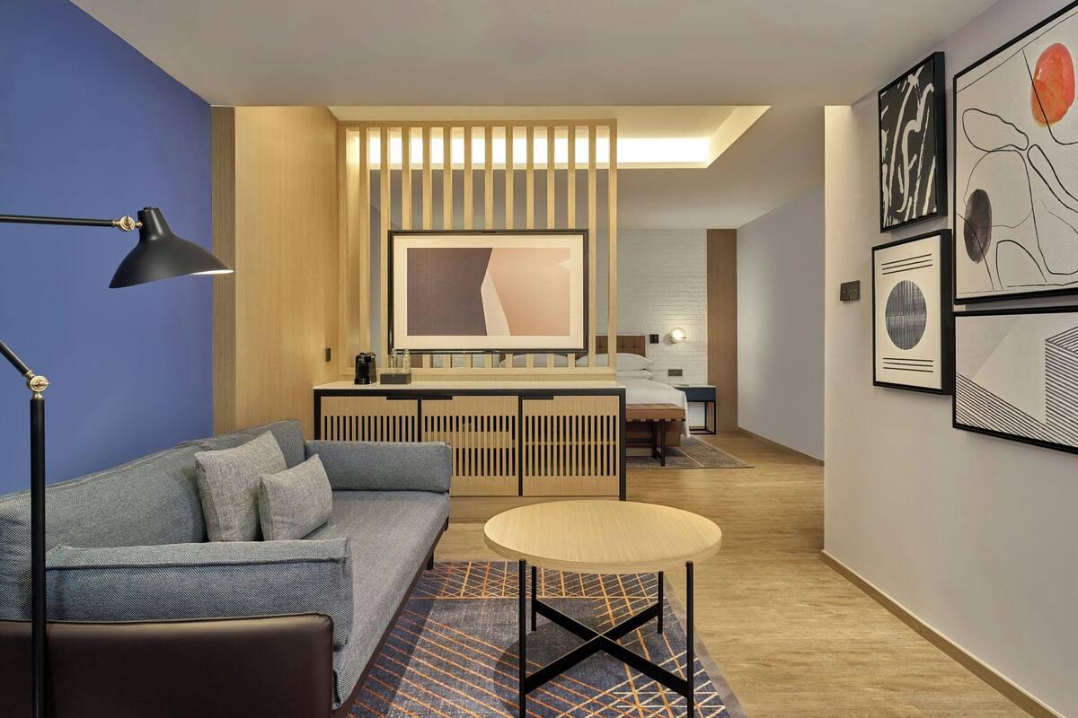 A modern hotel room with a sofa, a round table, a desk, and artwork on the walls.