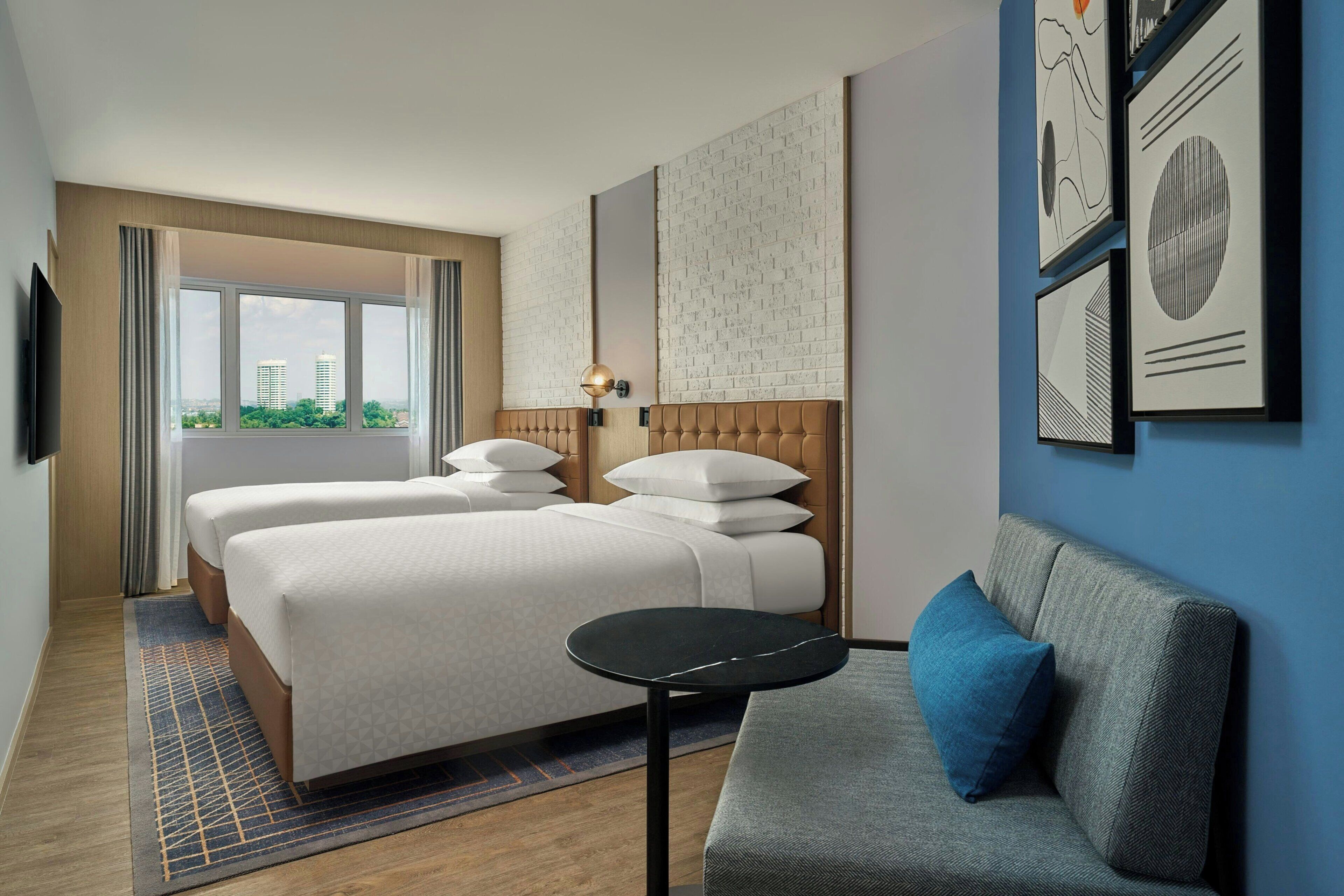 Ein Hotelzimmer mit zwei Betten, einem Schlafsofa, einem kleinen Tisch und Kunstwerken an den Wänden.
