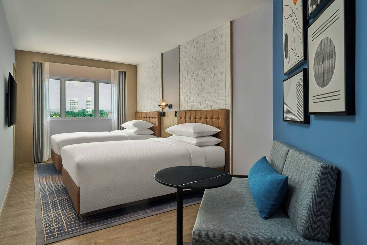 A hotel room with two beds, a sofa, a small table, and artwork on the walls.