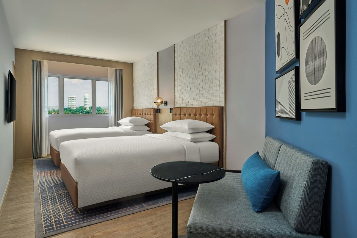 A hotel room with two beds, a sofa, a small table, and artwork on the walls.