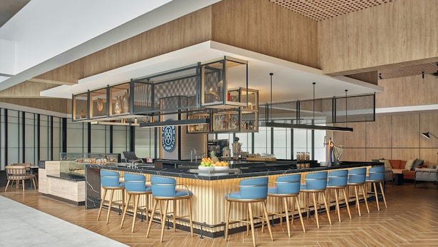 Una cocina moderna con una isla central, taburetes de bar y un alto techo con paneles de madera.