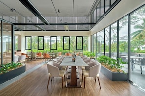 Una sala de reuniones moderna con una larga mesa, sillas cómodas y ventanas amplias que dan a vistas de espacios verdes y edificios.