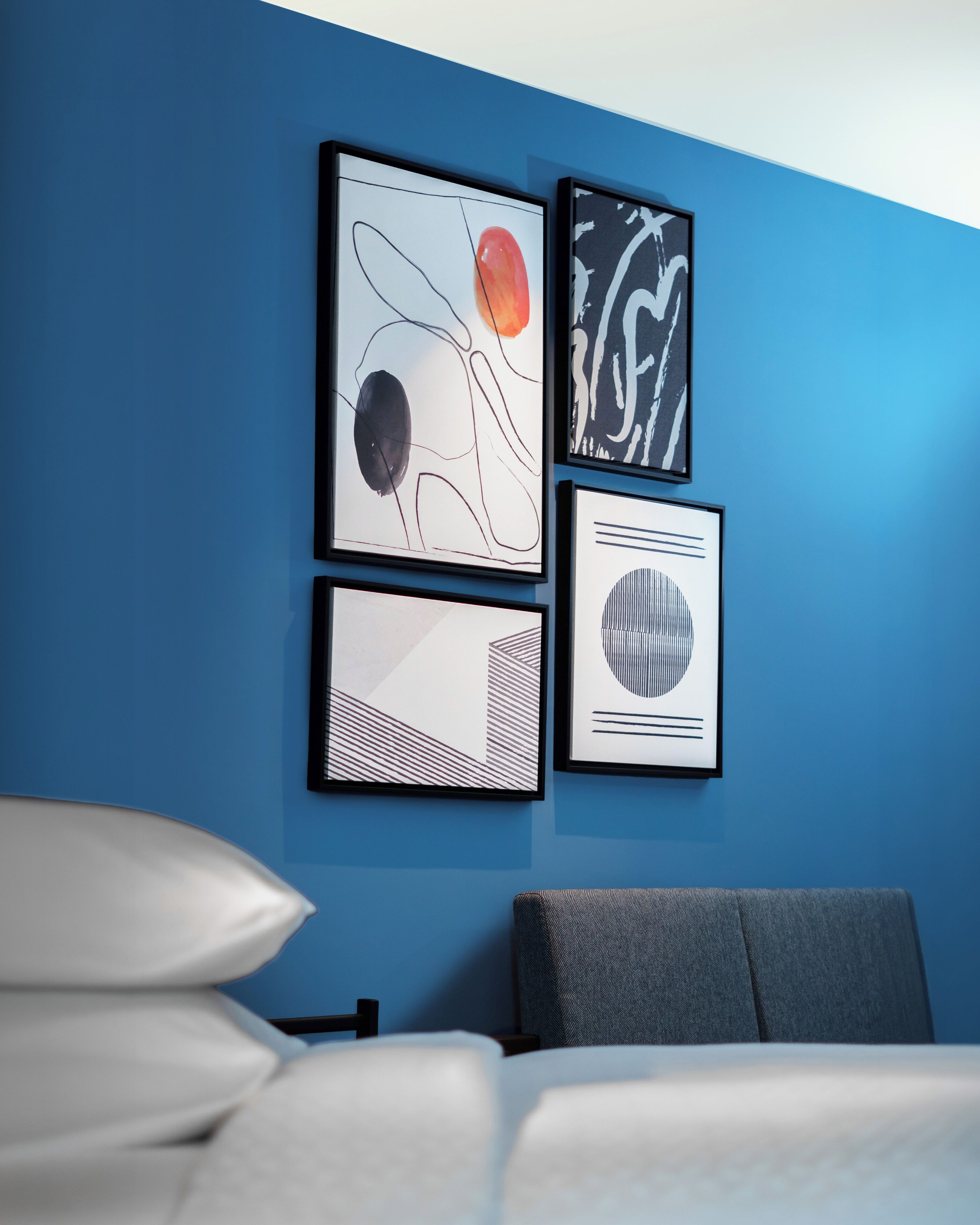 Una camera d'albergo con una parete blu, un letto con biancheria bianca e tre opere d'arte incorniciate.