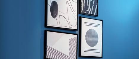 Una habitación de hotel con una pared azul, una cama con ropa de cama blanca y tres obras de arte enmarcadas.