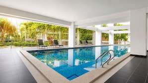 Una piscina con agua cristalina azul, rodeada de sillas de descanso y plantas en macetas, con vista a zonas verdes.