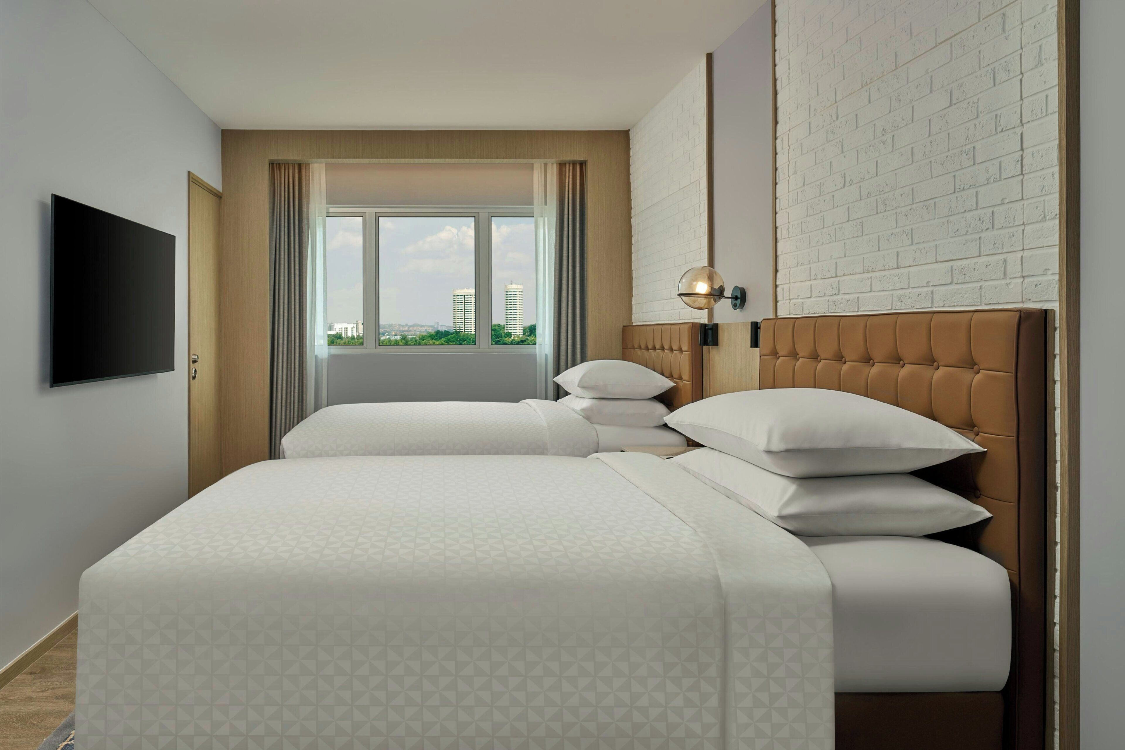 Ein Hotelzimmer mit Bett, Fernseher, Fenster mit Vorhängen und einer Backsteinwand.