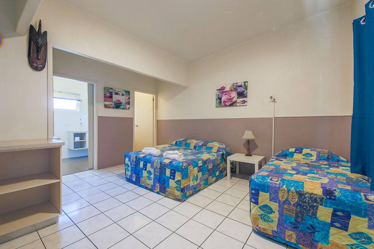 A room with two beds, a small table, a shelf, and a door leading to another room.