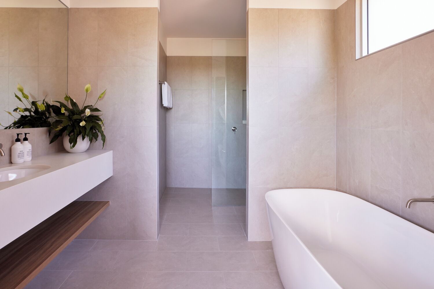 Un baño moderno con una bañera blanca, un tocador con espejo y una planta en maceta.