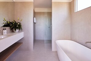 A modern bathroom with a white bathtub, a vanity with a mirror, and a potted plant. - The Hide Byron Bay (Byron Bay)
