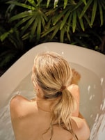 Una persona en una bañera con agua, rodeada de follaje.