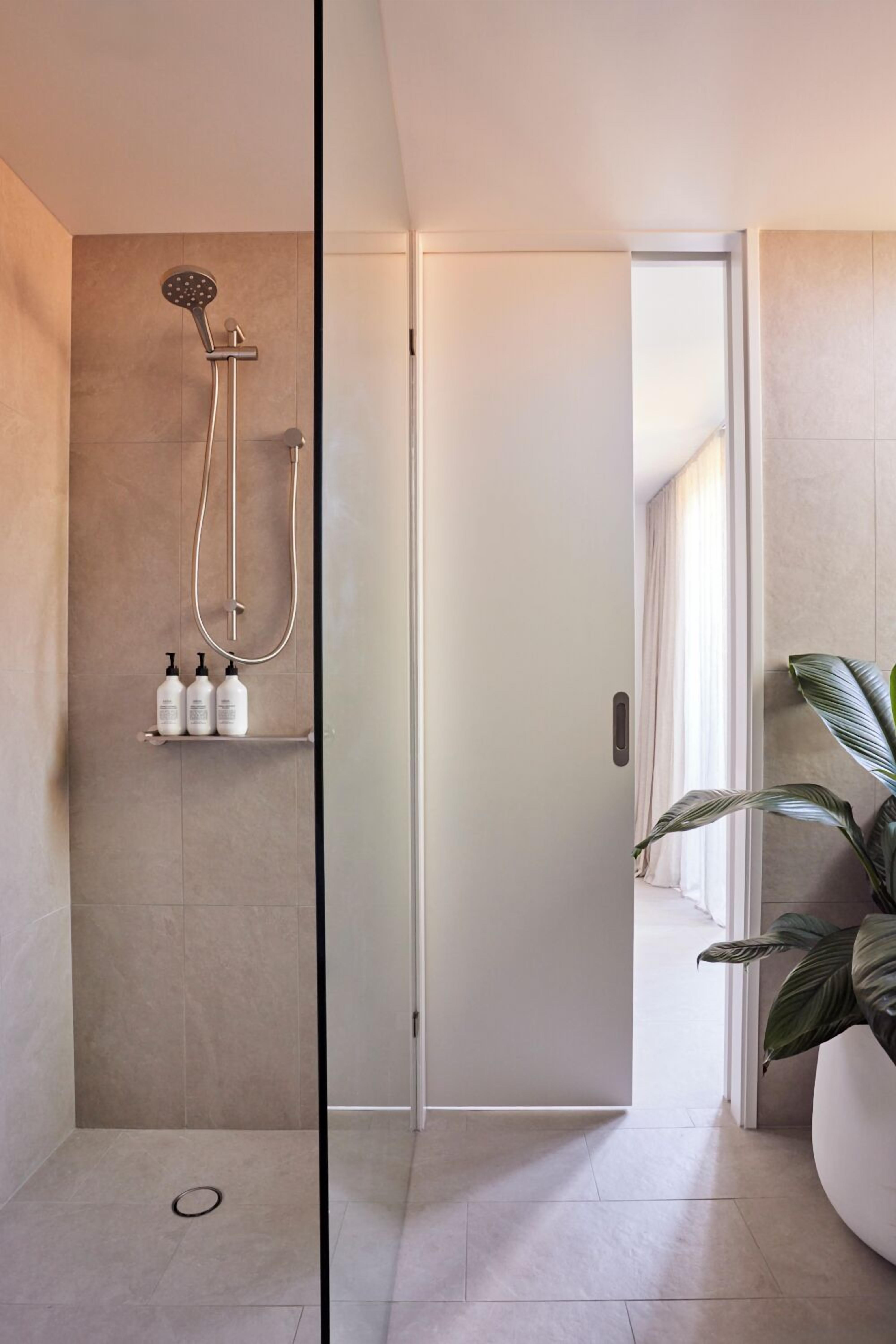 Un baño moderno con cabina de ducha de vidrio, una puerta blanca y una planta en maceta.