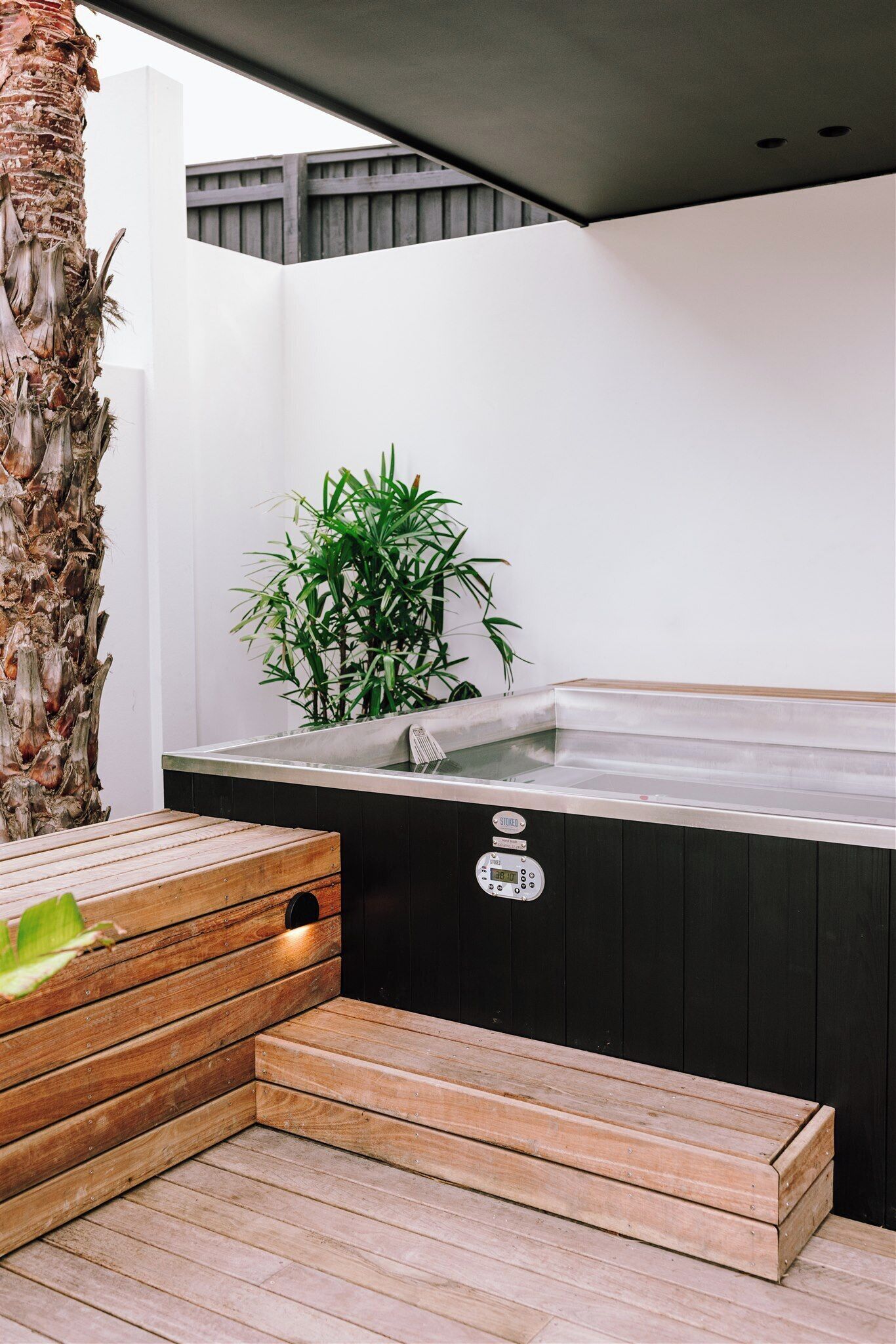 A modern outdoor hot tub area with a wooden bench, a bamboo plant, and a black hot tub.