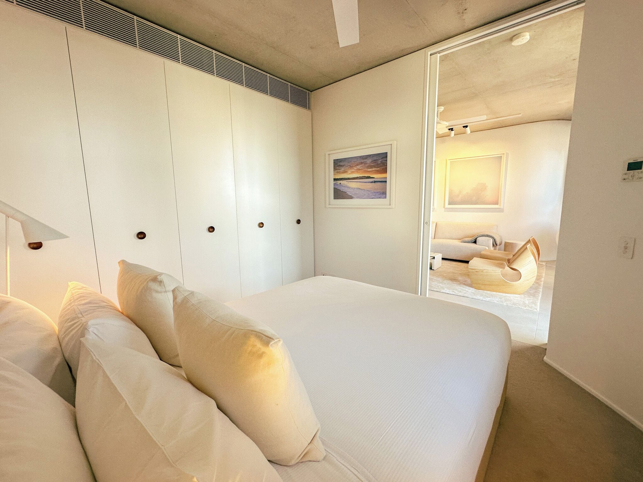 A modern bedroom with a large bed, a walk-in closet, and a bathroom visible through an open door.