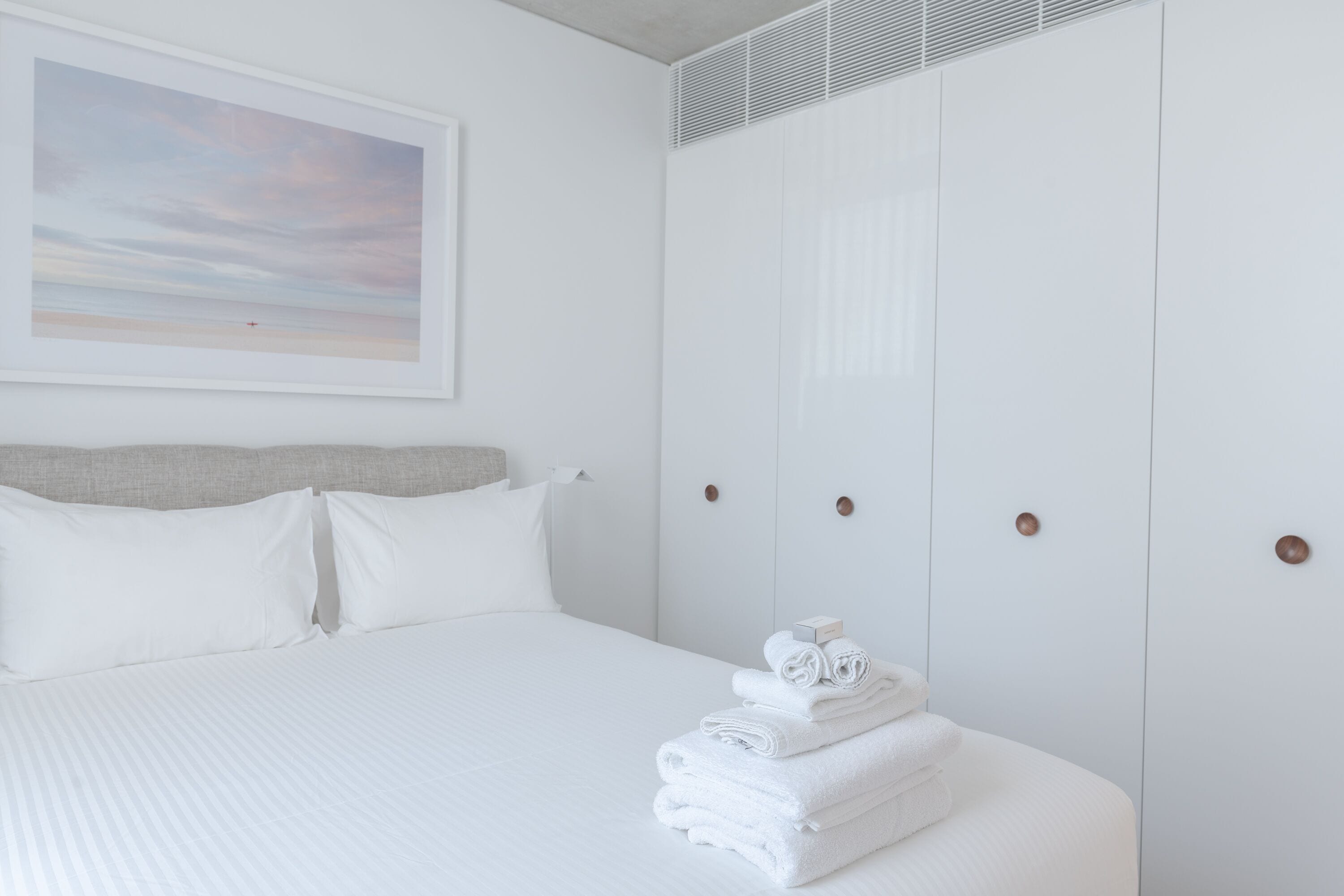 A neatly made bed with white linens, a headboard, and a framed picture on the wall.