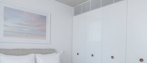 Een net opgemaakt bed met witte lakens, een hoofdbord en een ingelijst beeld aan de muur.