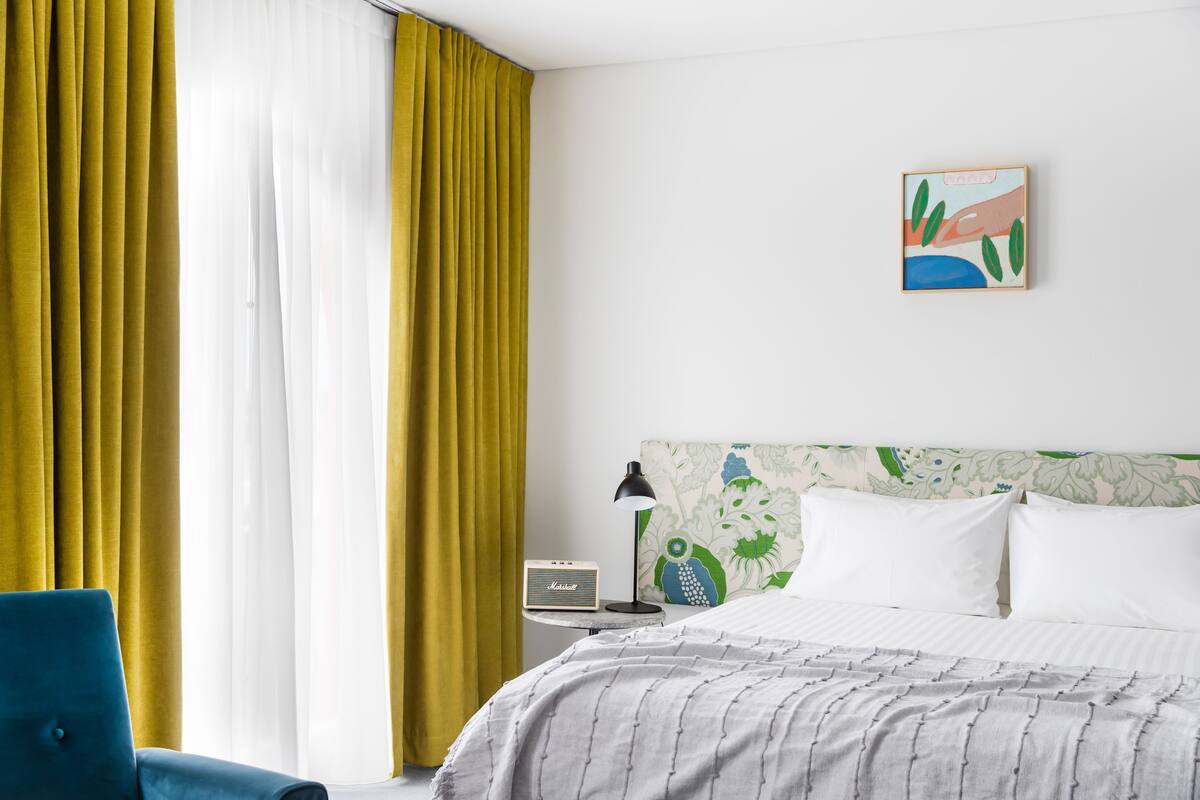 A hotel room with a bed, a chair, a nightstand with a lamp, and a painting on the wall.