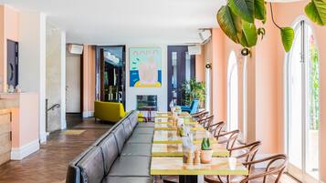 A modern restaurant with a long communal table, cushioned seating, and large windows.