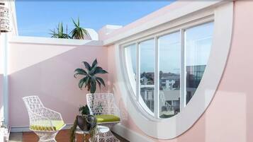 Un balcon avec deux chaises en osier blanches, une petite table ronde et une plante en pot.