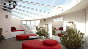 A modern interior with a curved ceiling, red seating, and potted plants. - Hotel Ravesis (Bondi Beach)