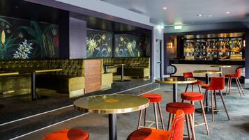 A bar area with high stools and a bar counter, featuring a mural of tropical plants on the wall.