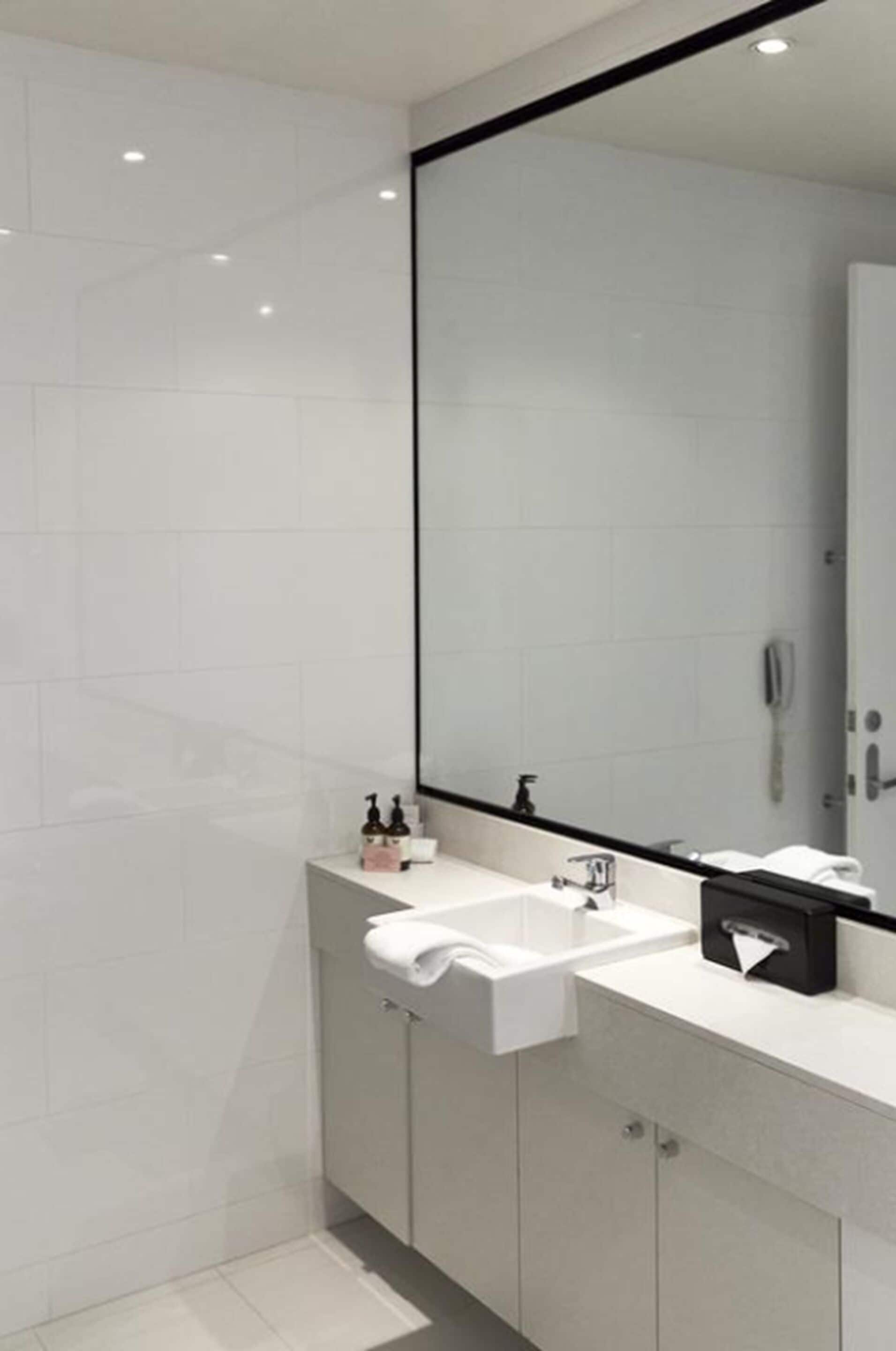 A modern bathroom with a large mirror, white tiles, a white sink, and a towel rack.