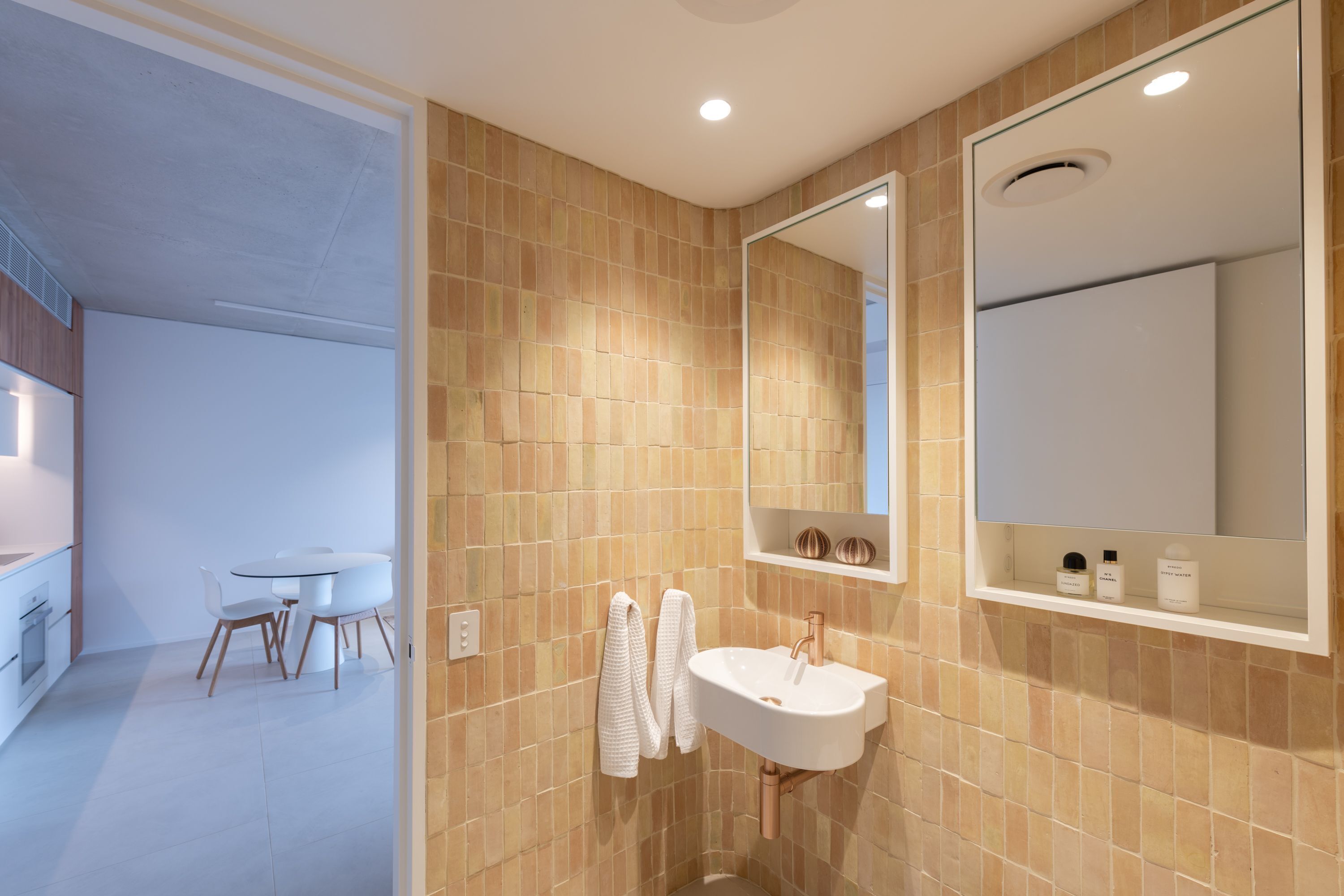 A modern bathroom with beige tiles, a white sink, and a large mirror.