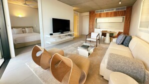 A modern living room with a sofa, coffee table, and chairs. There is a flat-screen TV mounted on a white console. The room has a ceiling fan and a wooden accent wall. - Hotel Ravesis (Bondi Beach)