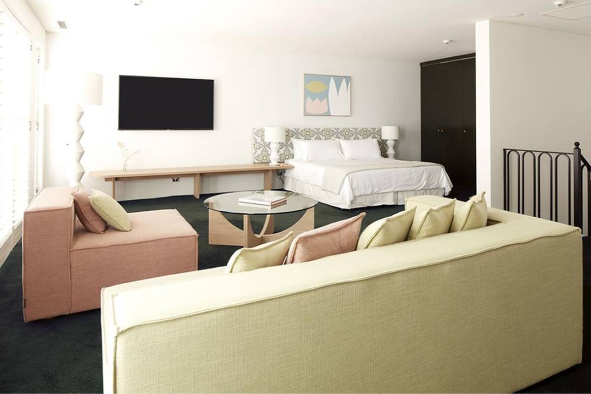 A hotel room with a bed, a sofa, a small table, and a TV on the wall.