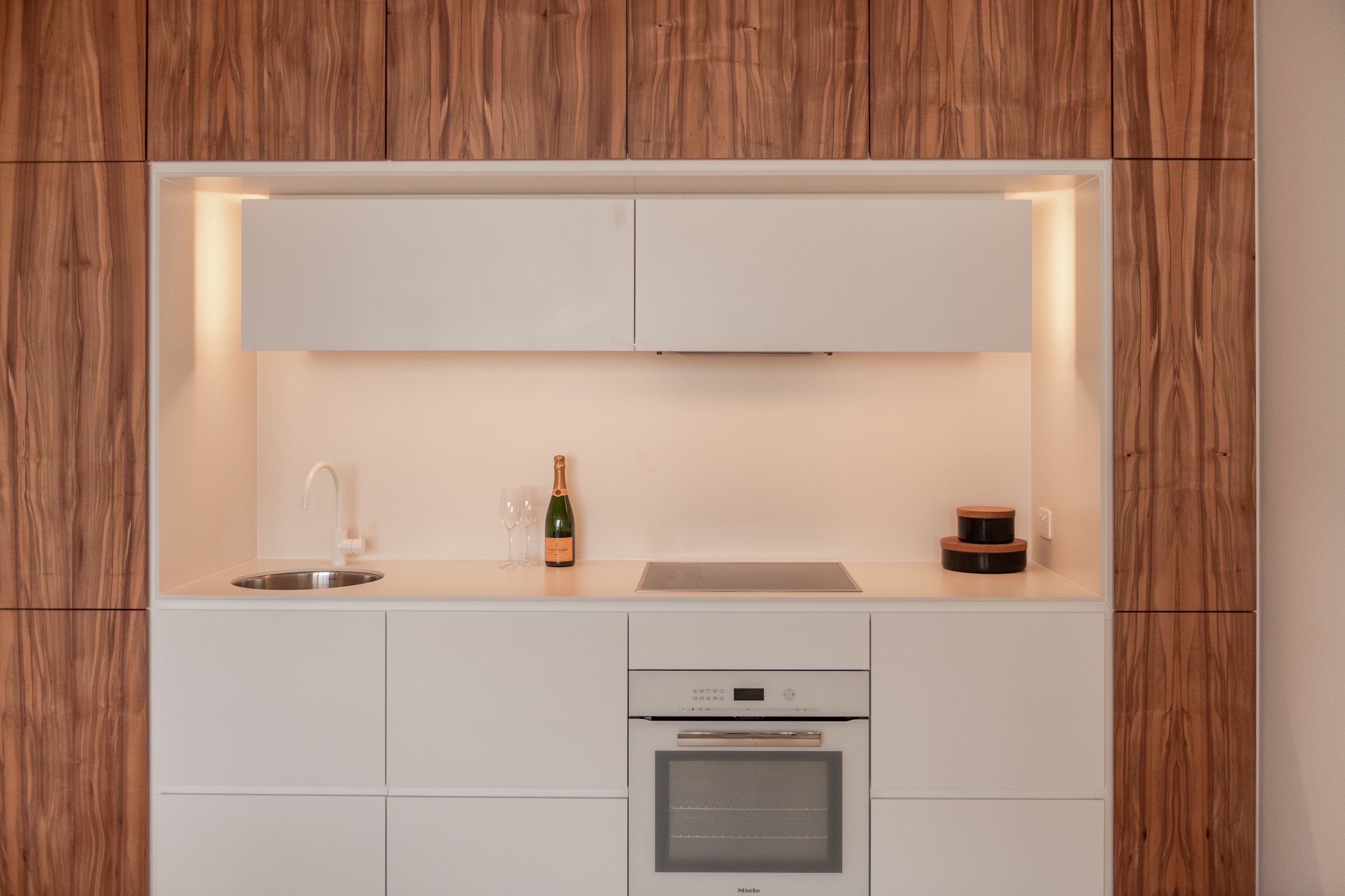 Een moderne keuken met witte kasten, een inbouwoven en een wijnfles op het aanrecht.