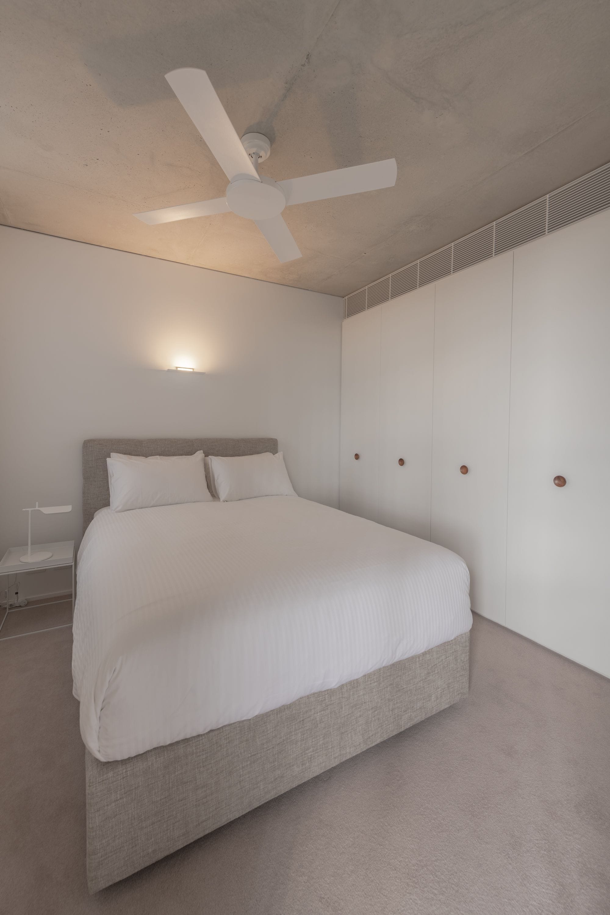 Un dormitorio con cama, ventilador de techo, mesita de noche y armario.