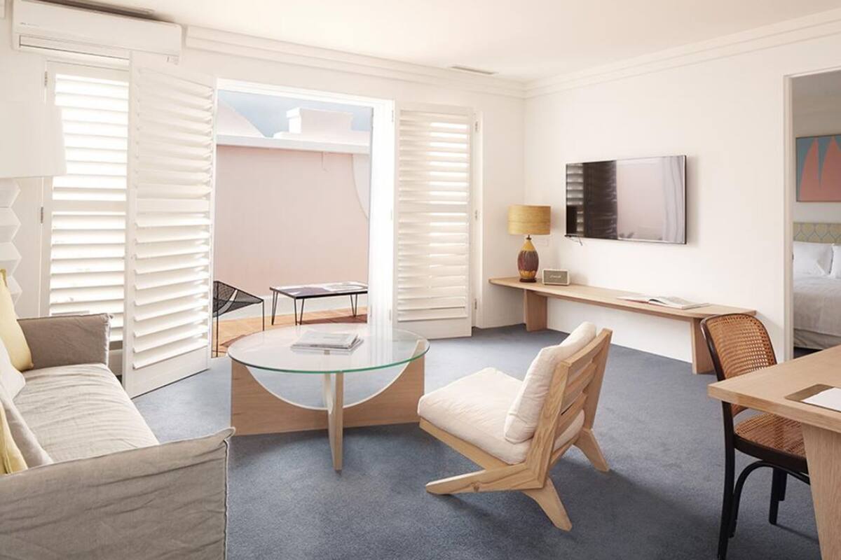 A modern hotel room with a glass table, a sofa, a desk, and a TV.