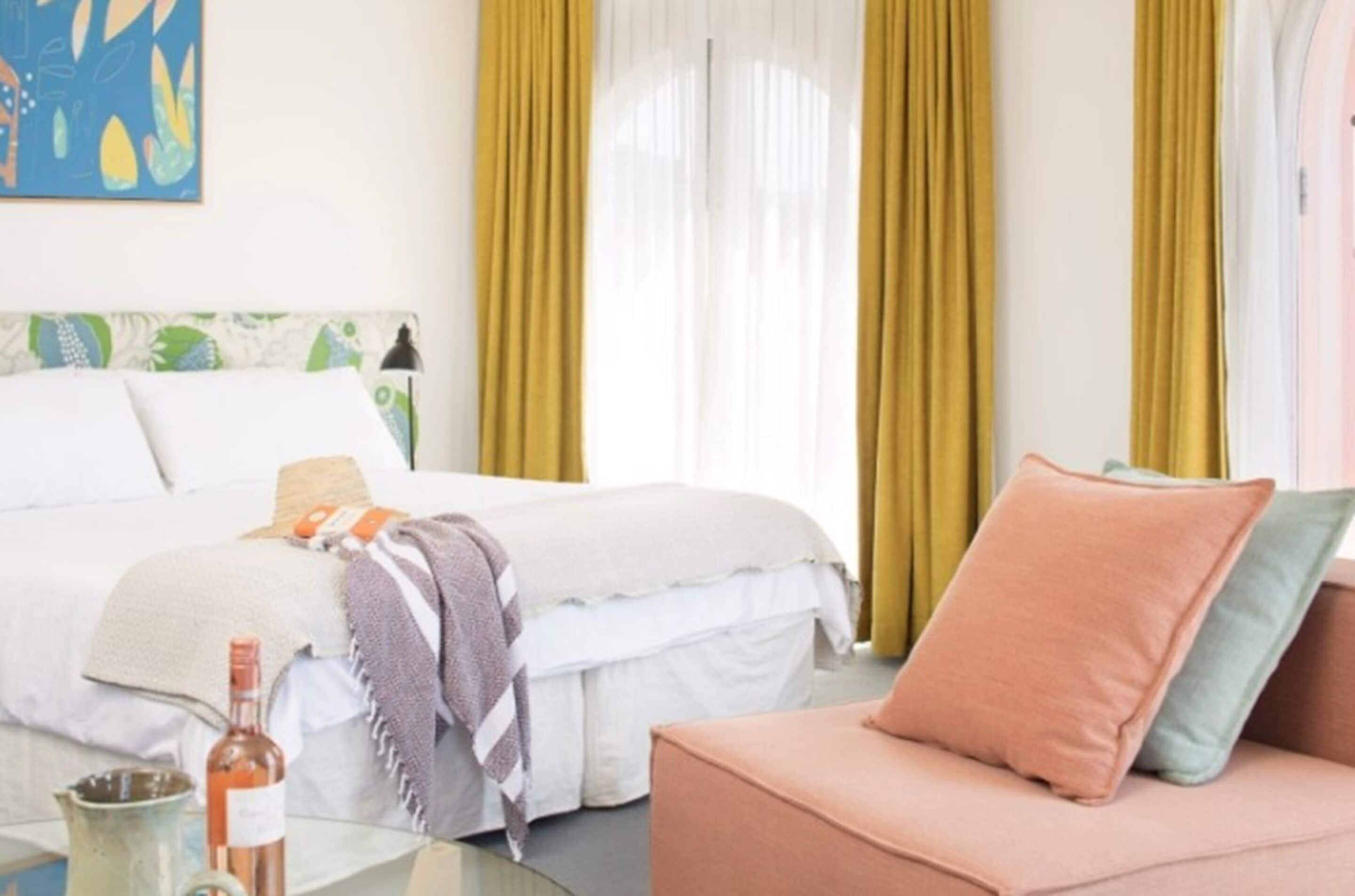 A hotel room with a bed, a sofa, a table with a bottle, and curtains.