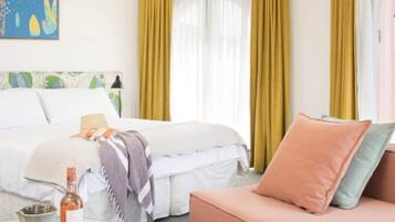 A hotel room with a bed, a sofa, a table with a bottle, and curtains.