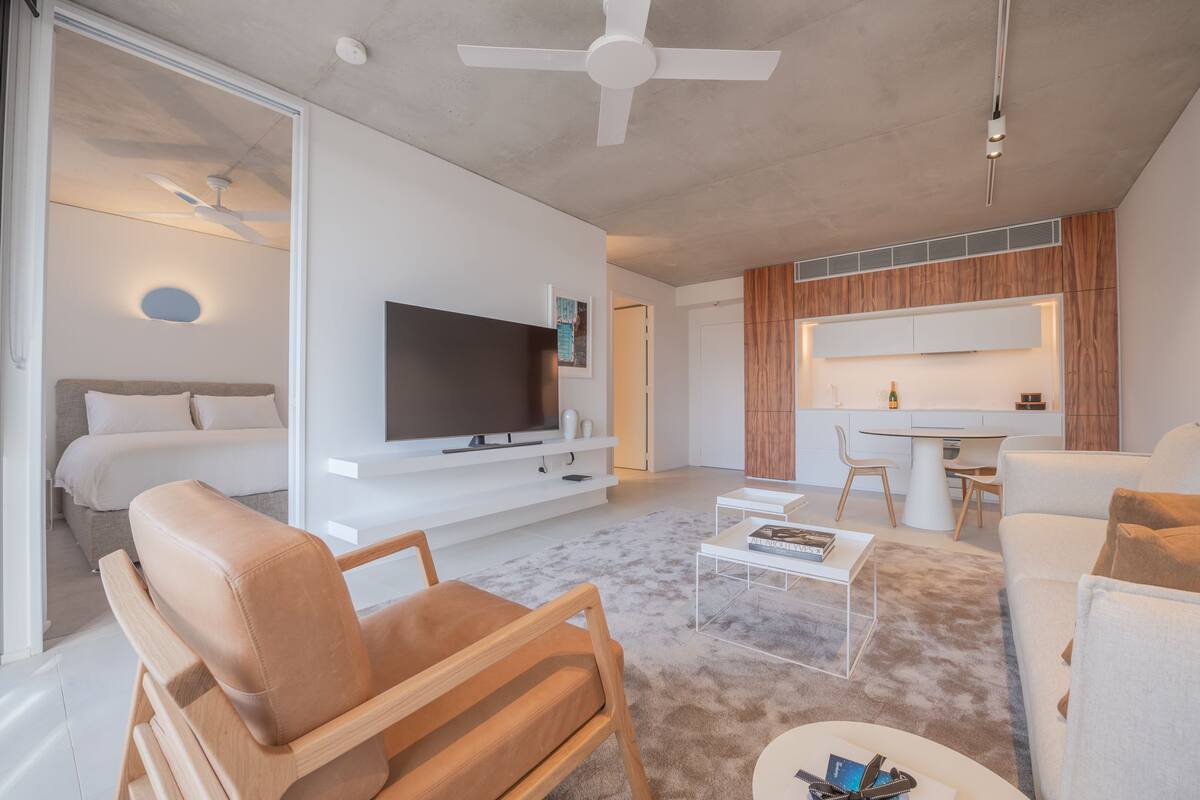 A modern living room with a flat-screen TV, a dining area, and a kitchen.