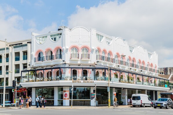 A hotel with a white facade, multiple balconies, and a sign reading "RALESI'S CORNER 1914".