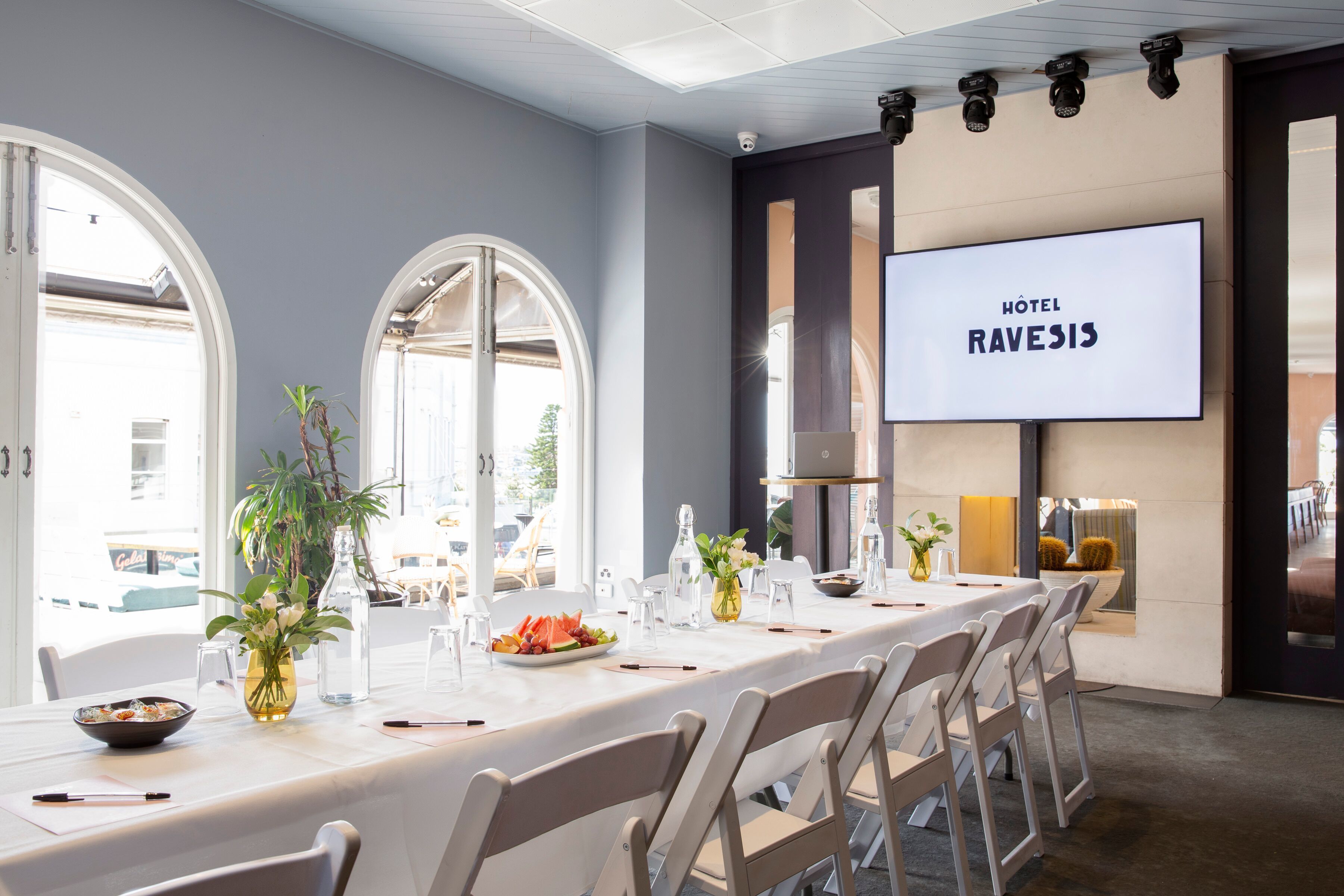 Un salón de conferencias de hotel con una larga mesa, sillas y una gran pantalla mostrando 