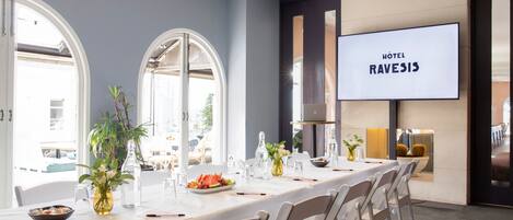 Un salón de conferencias de hotel con una larga mesa, sillas y una gran pantalla mostrando
