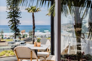 A balcony with wicker chairs and a table, overlooking a beach and ocean.