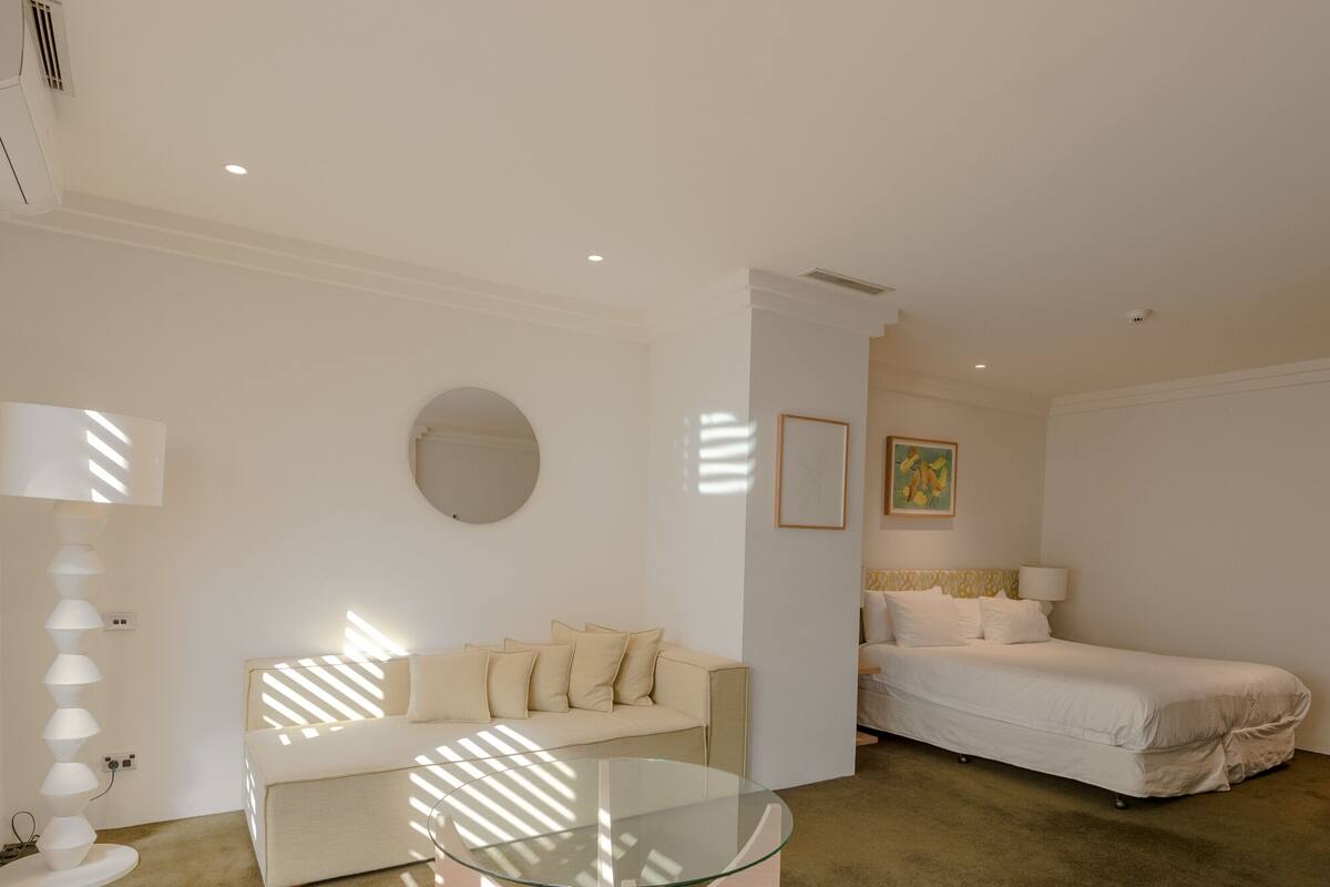 A modern hotel room with a large bed, a sofa, a glass coffee table, and a floor lamp.